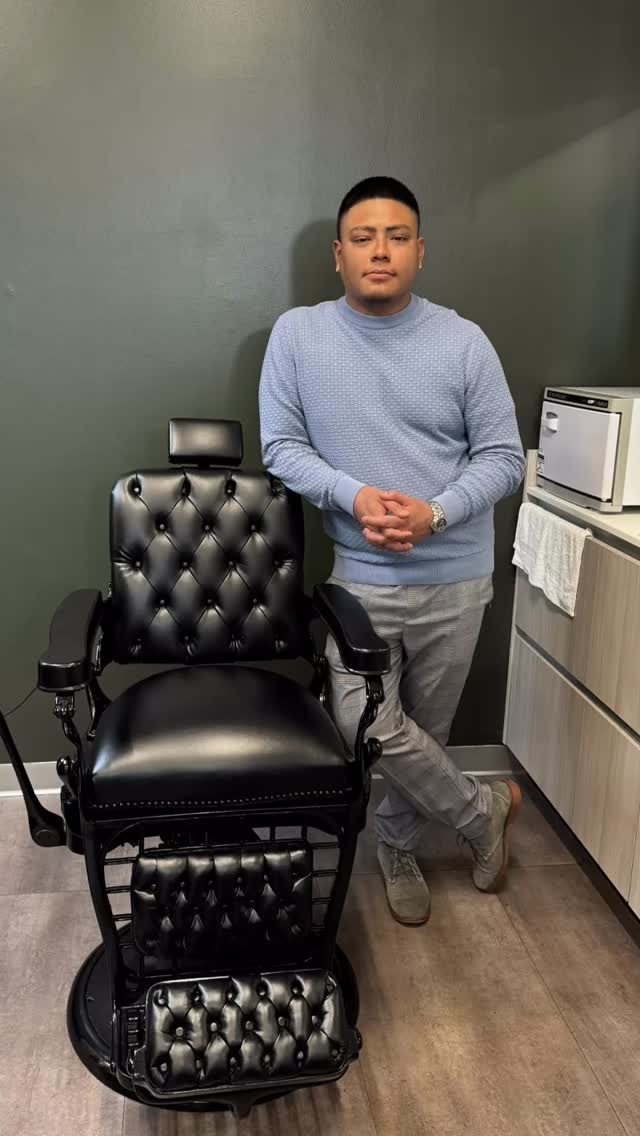 A black tufted barber chair and a man in the parlor against a green wall